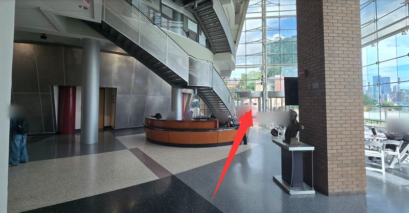Babbio Center lobby with a round front desk; a red arrow points to the glass doors