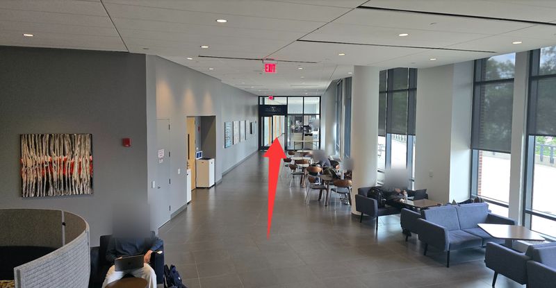 Lower-level corridor with seating; a red arrow points to glass doors at the far end